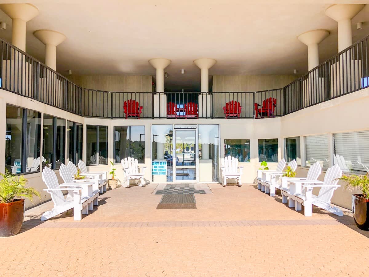 Top Of The Gulf 621 – Outdoor seating area with white adirondack chairs and a view of entry doors to the building.
