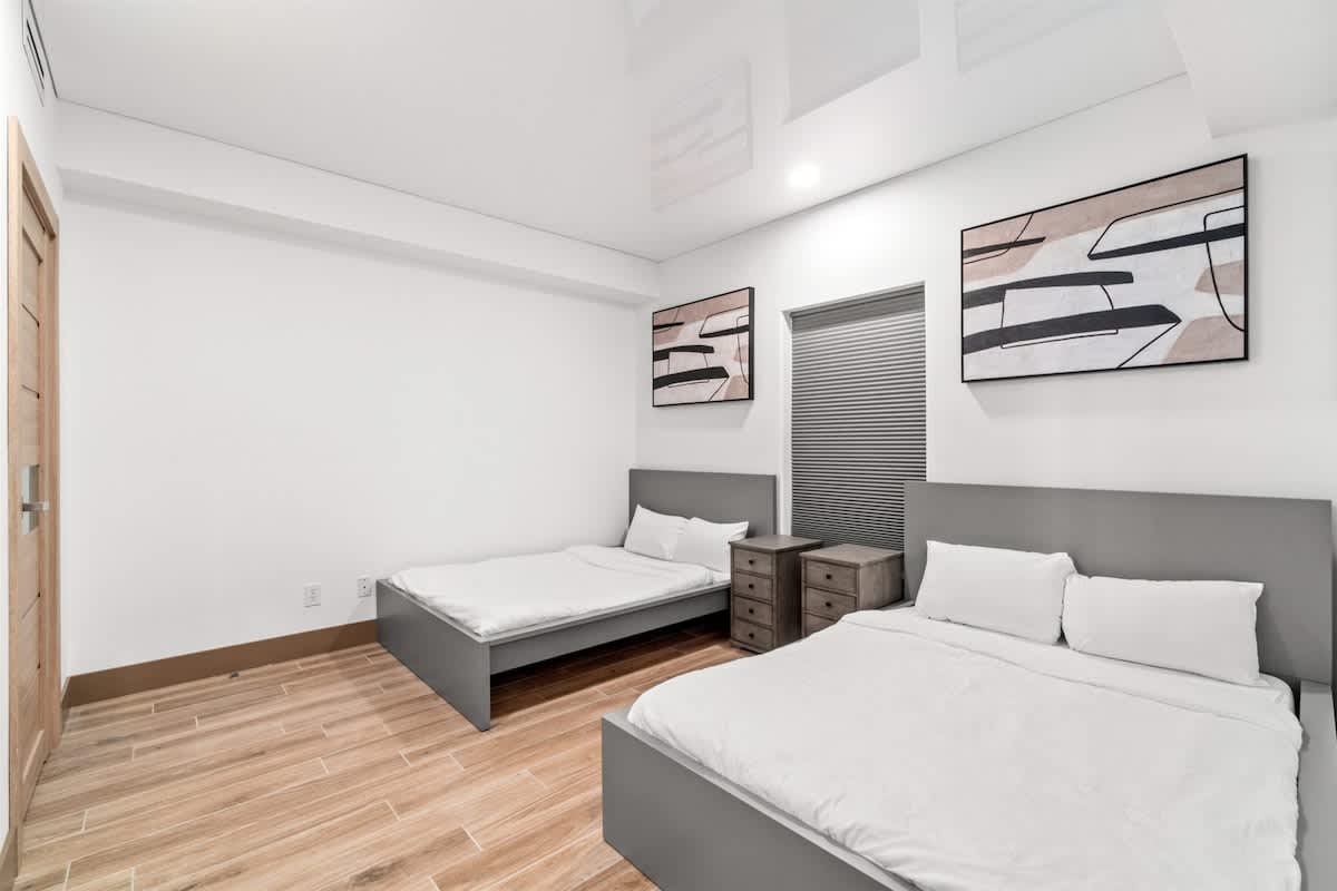 Ocean Villa 1302 – Bedroom with two beds, wooden floor, modern decor, and window with blinds.