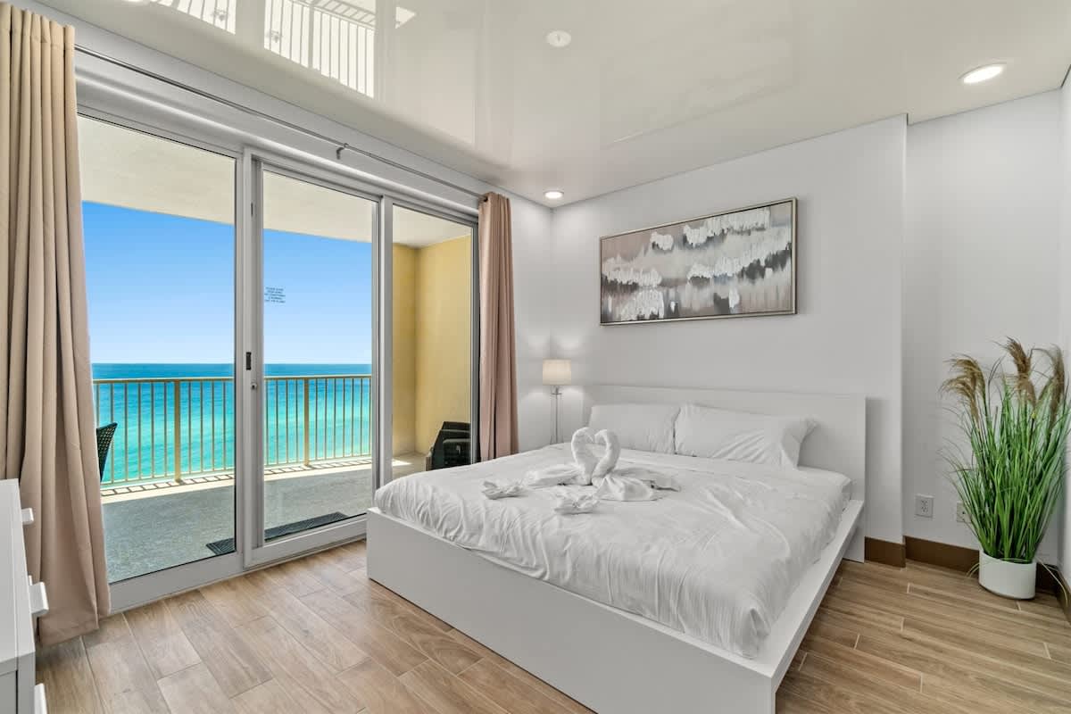 Ocean Villa 1302 – Bedroom with white bed, ocean view balcony, and decorative wall art.