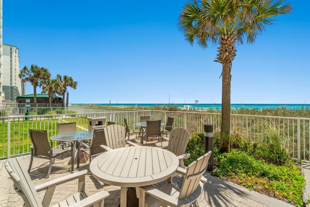 Ocean Villa 1302 – Seaside patio with tables, chairs, palm trees, and ocean view.