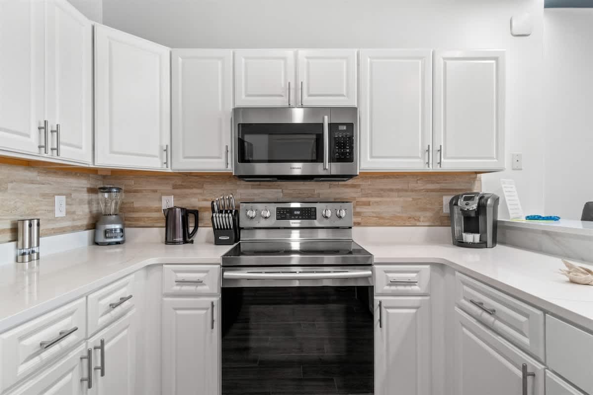 Ocean Villa 1302 – Modern kitchen with stainless steel appliances, white cabinets, and a view of the dining area.