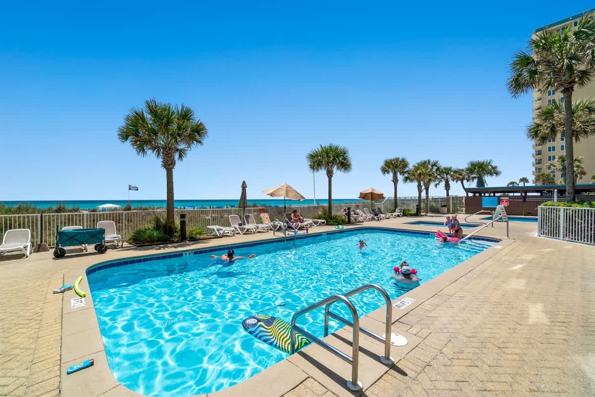 Ocean Villa 1302 – Swimming pool surrounded by palm trees with ocean view, sun loungers, and umbrellas.