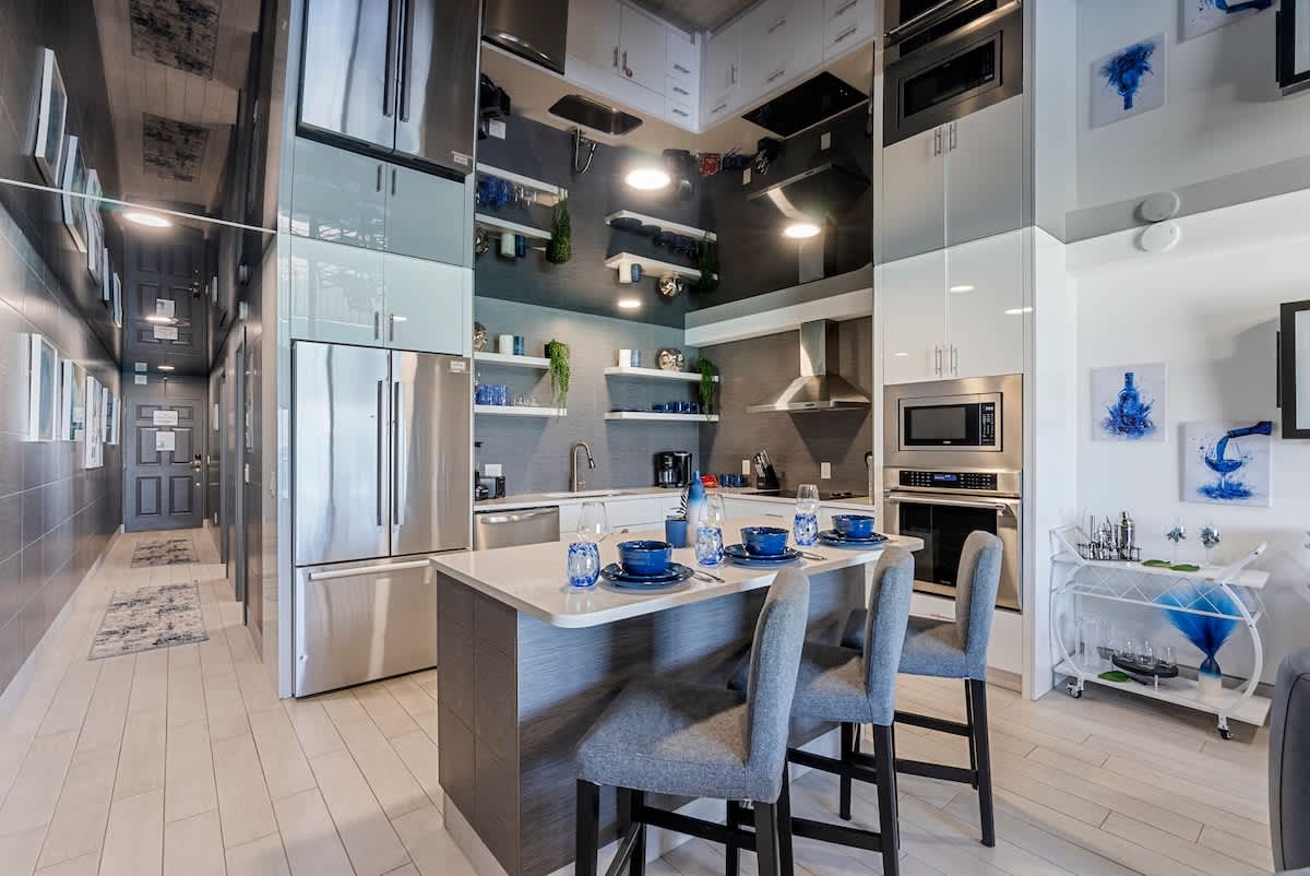 The Summit 1205 – Modern kitchen with stainless steel appliances, gray cabinets, and a dining area with blue dishware.