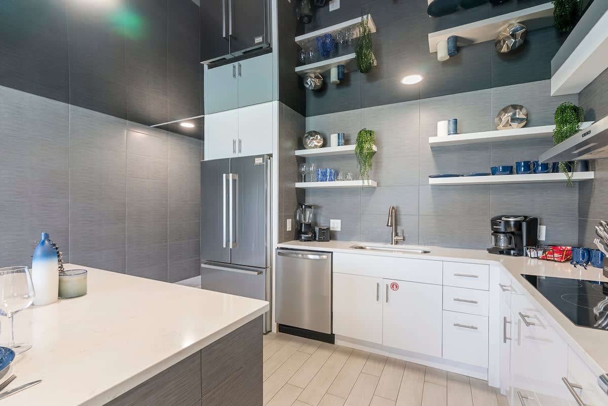 The Summit 1205 – Modern kitchen with stainless steel appliances, white cabinetry, and decorative shelving, featuring a light wood floor.
