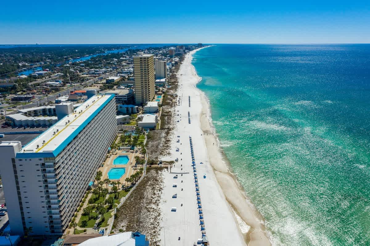 The Summit 1205 – Aerial view of a beach with white sand, pools, and a hotel along the shoreline.