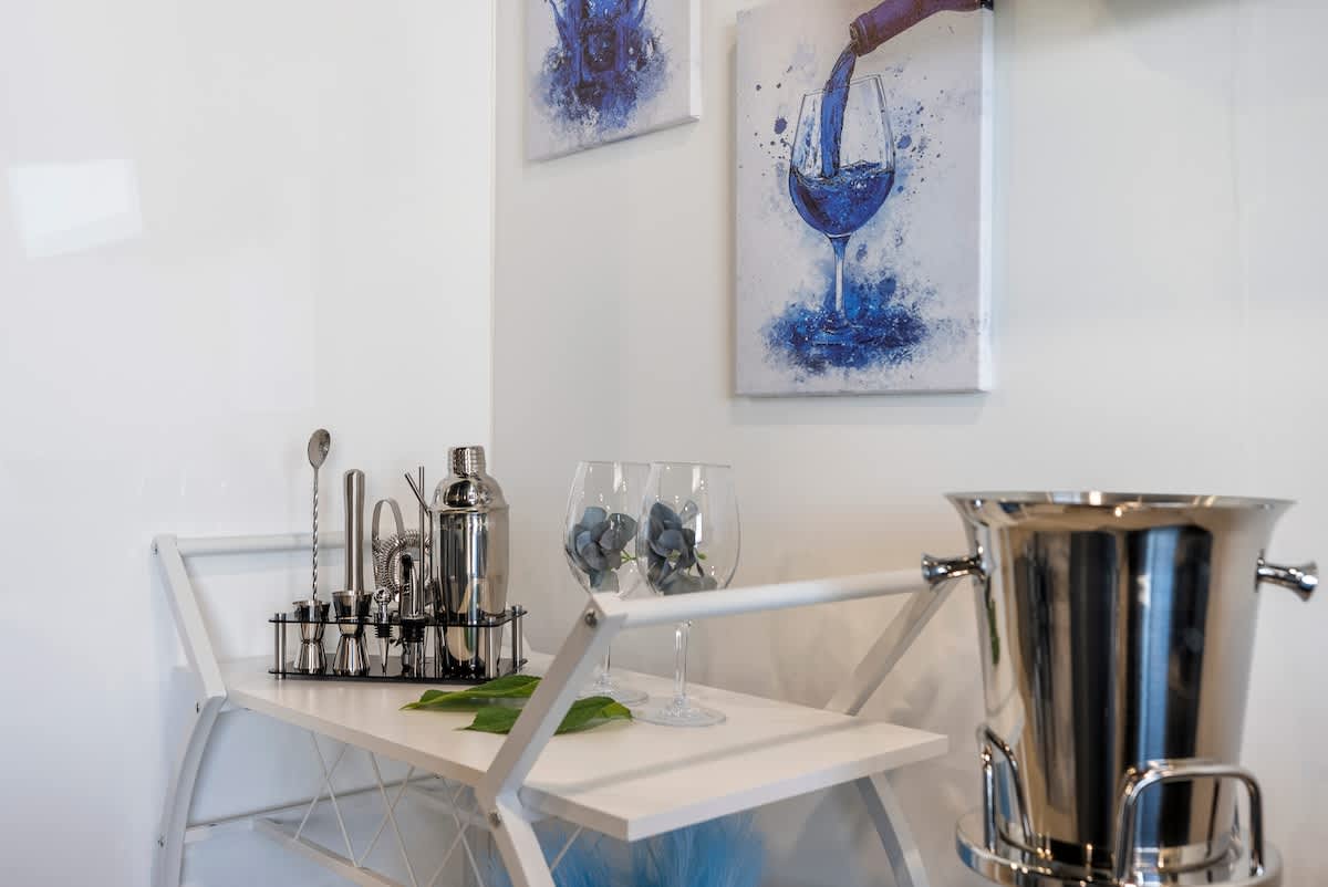 The Summit 1205 – Bar cart with cocktail tools, decorative glasses, and paintings of wine glasses on a white wall.