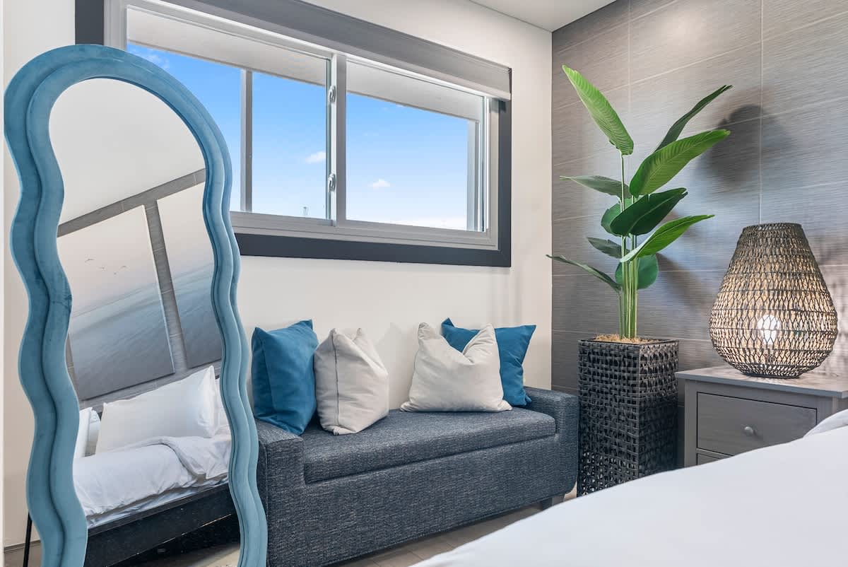 The Summit 1205 – Cozy bedroom corner with a blue mirror, couch, tropical plant, and window view.