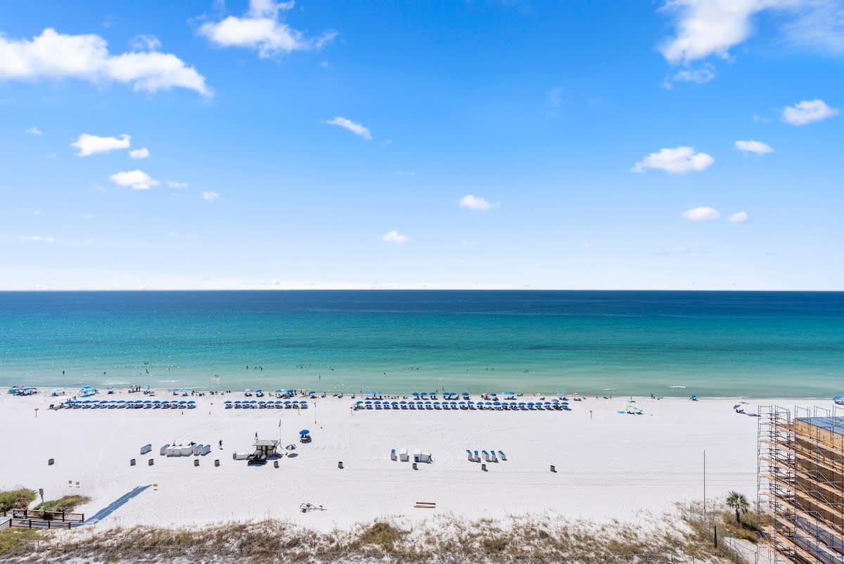 The Summit 1205 – Ocean view from balcony with white sand beach, umbrellas, and clear blue water.