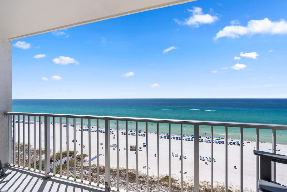 The Summit 1205 – Balcony view overlooking sandy beach, ocean, and blue sky with lounge chairs visible on the shore.