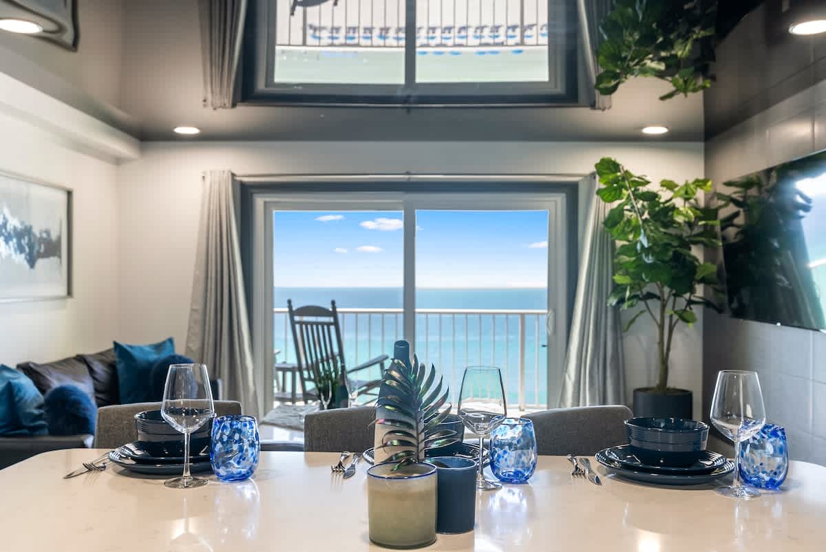 The Summit 1205 – Dining area with ocean view, modern decor, table set with blue dishware, and a potted plant.