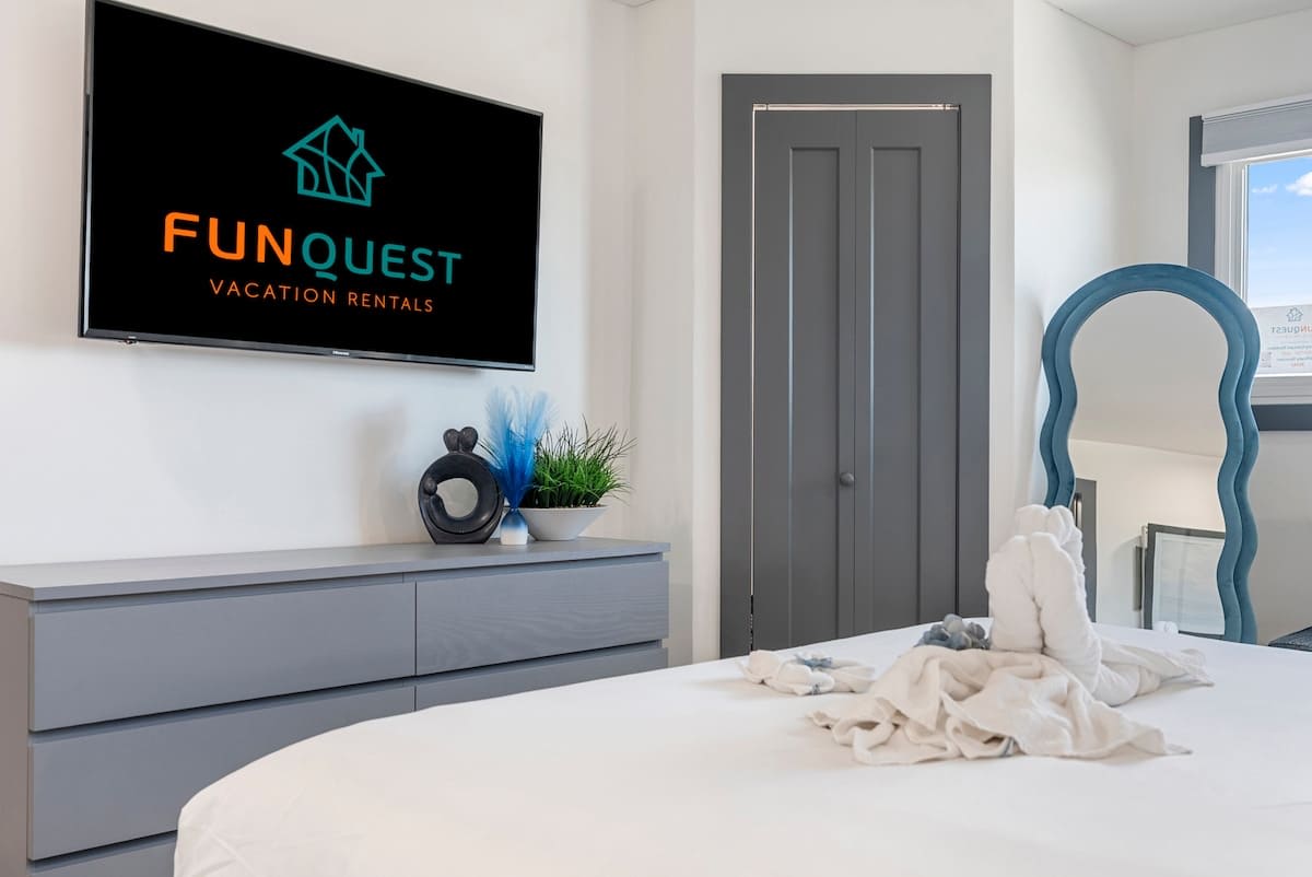 The Summit 1205 – Bright bedroom with a bed, dresser, TV, decorative mirror, and indoor plants.