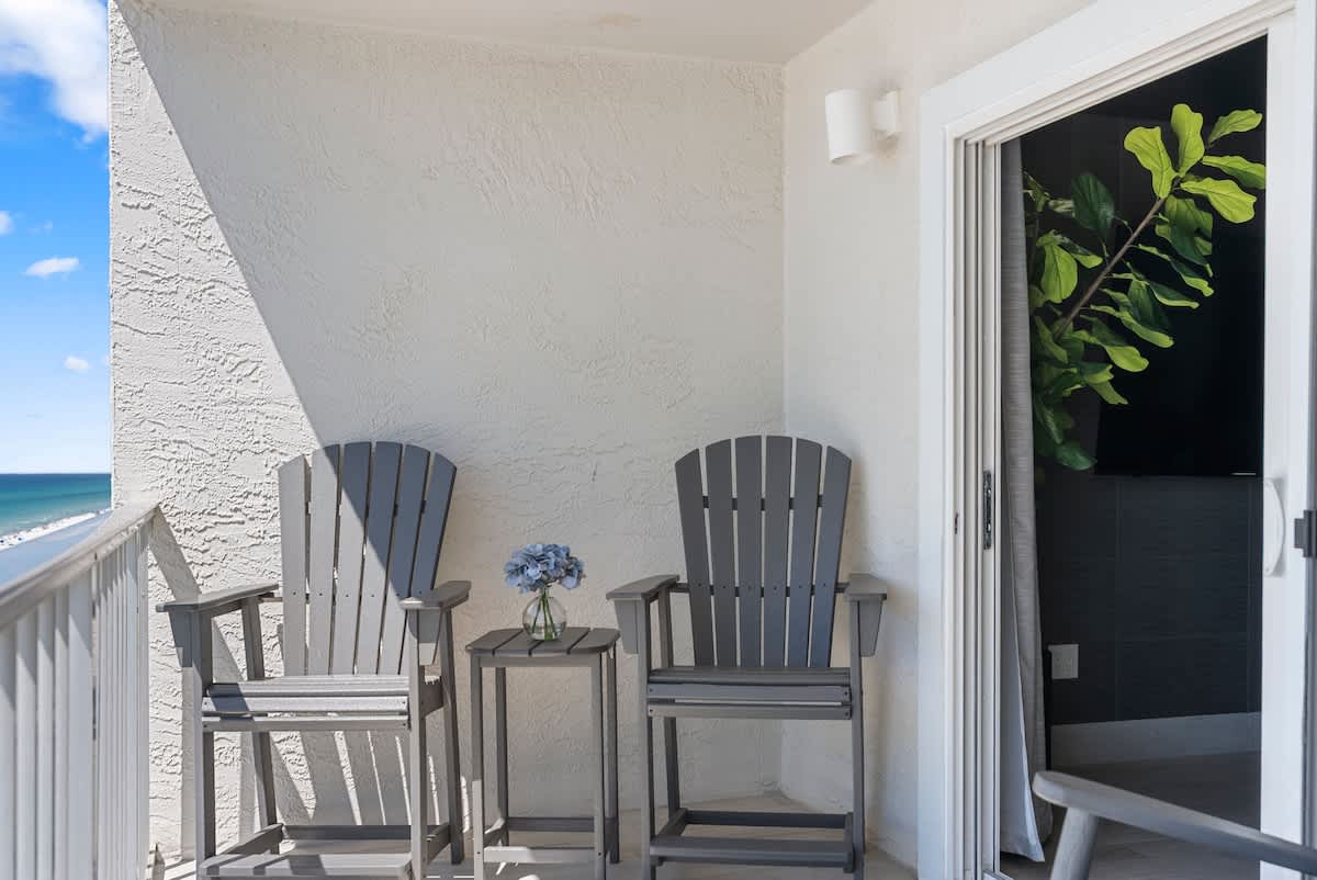 The Summit 1205 – Two gray Adirondack chairs and a table on a balcony with ocean view.