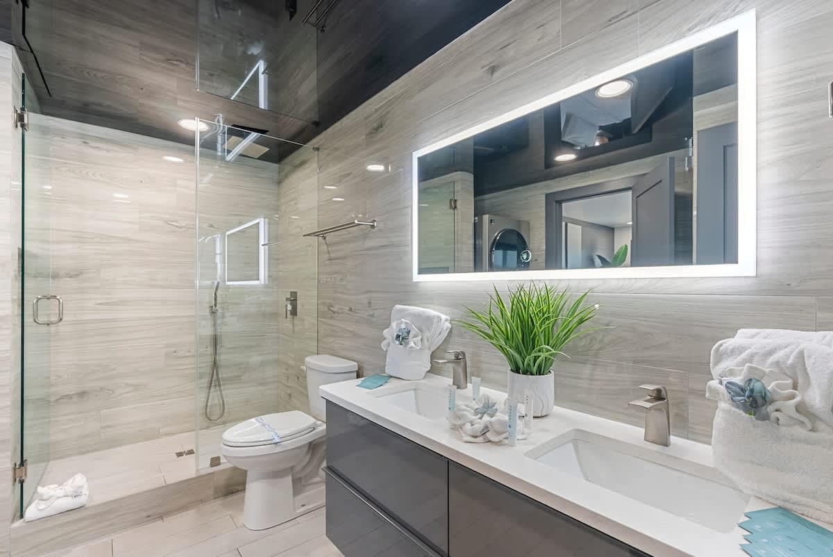 The Summit 1205 – Modern bathroom with glass shower, double vanity, plants, and gray tile accents.