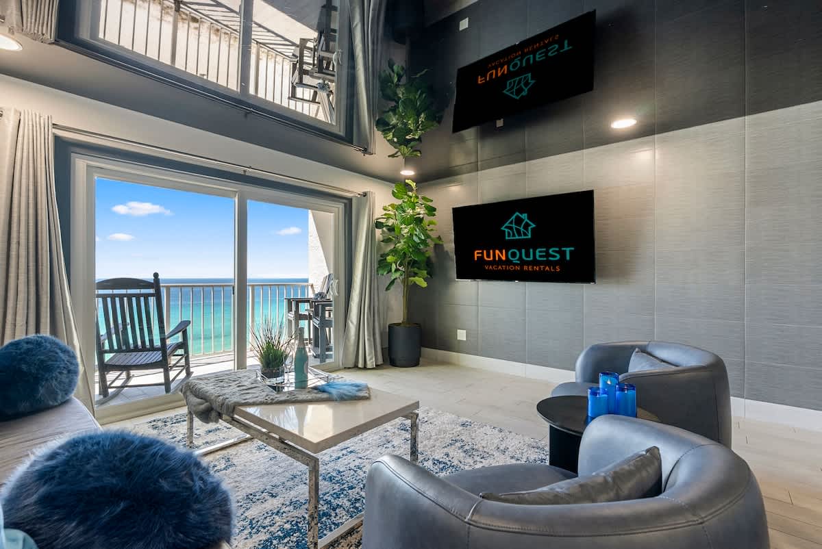 The Summit 1205 – Living room with ocean view, balcony access, two TVs, modern decor, and a blue rug.