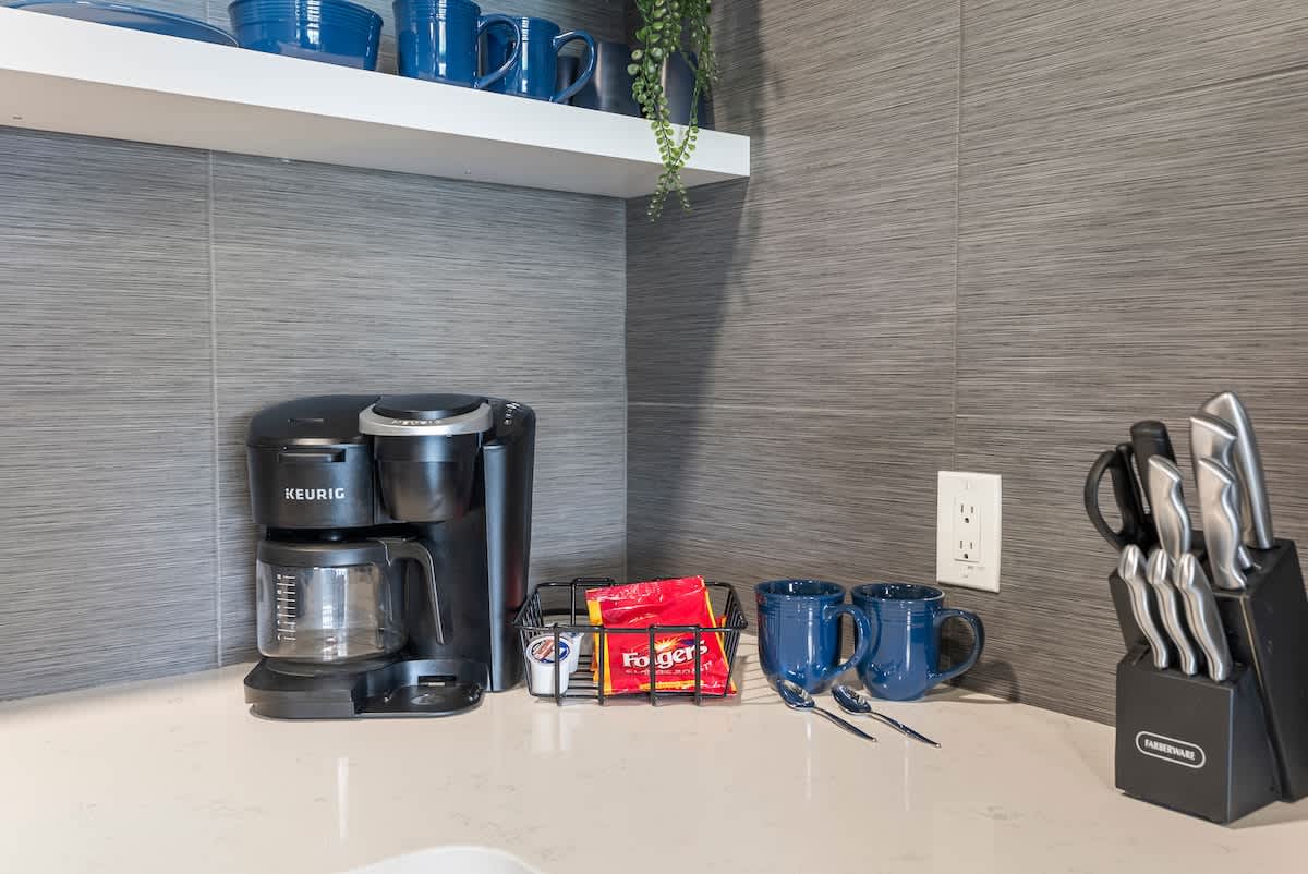 The Summit 1205 – Coffee station with Keurig, mugs, coffee packets, and a knife set on a countertop.