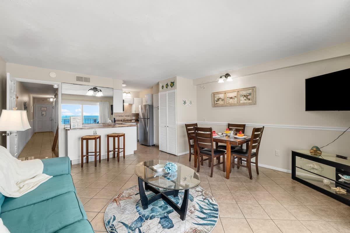 The Summit 1123 – Cozy living and dining area with table, kitchen bar, and ocean view through large window.