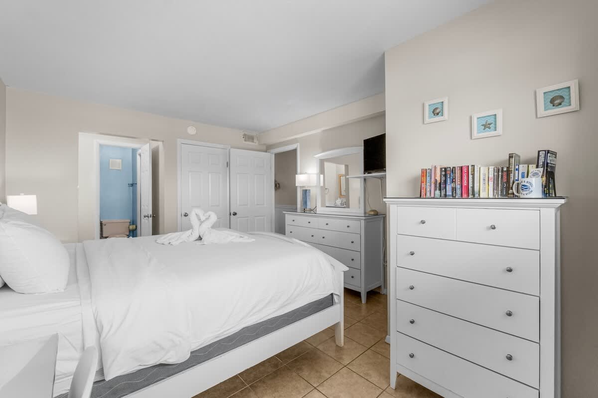 The Summit 1123 – Bedroom with a bed, dresser, TV, and open closet doors revealing a bathroom.