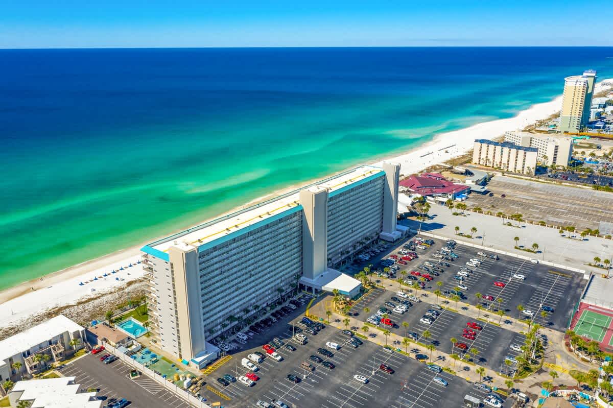 The Summit 1123 – Aerial view of The Summit 1123, beachfront property with turquoise water, white sand, and parking.