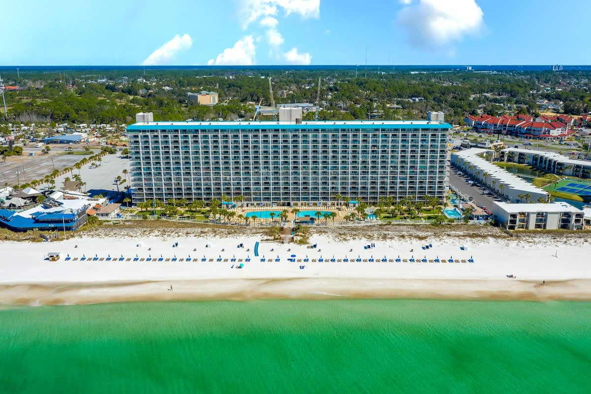 The Summit 1123 – Large beachfront hotel with pool, cabanas, and beach chairs along white sand.