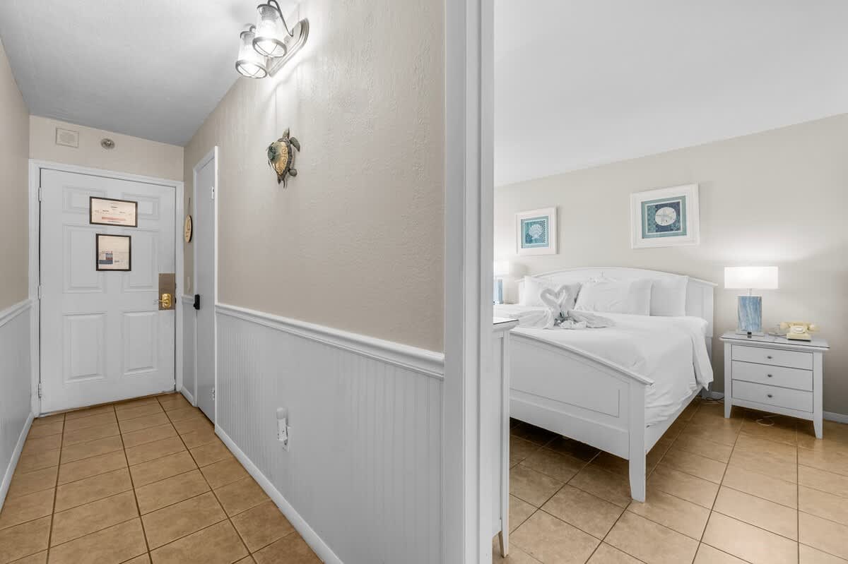 The Summit 1123 – Entryway leading to a bright bedroom with a white bed, nightstand, and ceramic tile floor.