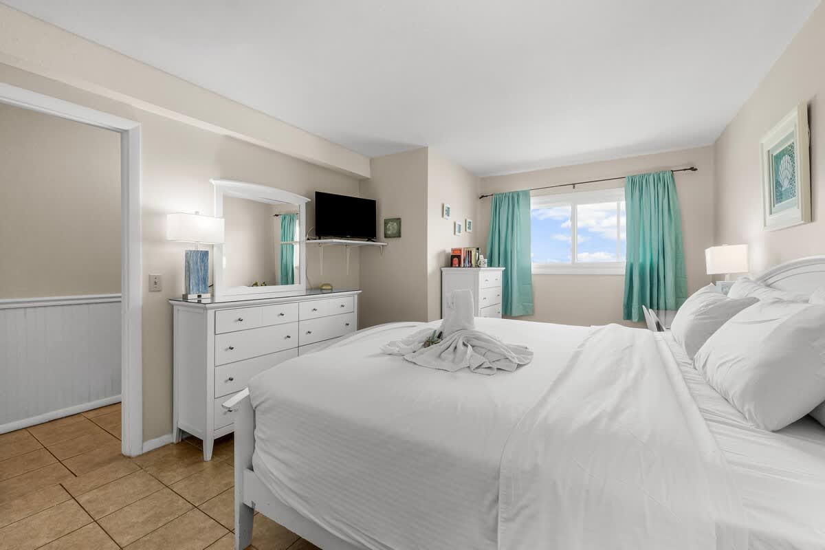 The Summit 1123 – Cozy bedroom with a queen bed, dresser, TV, and large window with turquoise curtains.