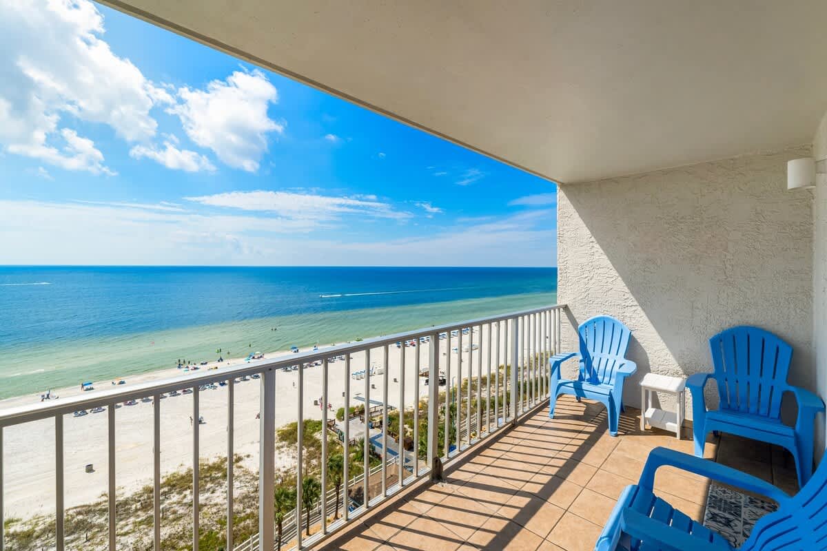The Summit 1123 – Balcony view of the beach with blue chairs and ocean below.