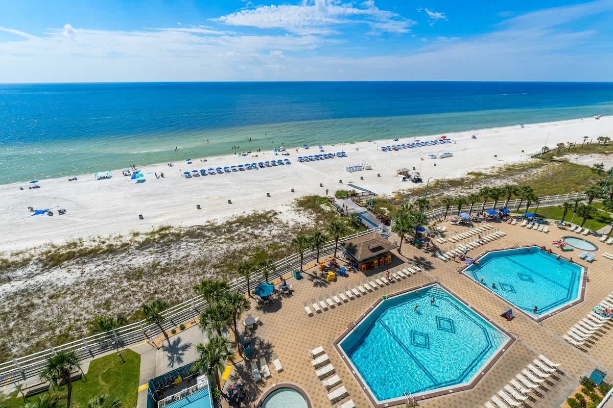 The Summit 1123 – Ocean view from a balcony overlooking pools and beach umbrellas on a sandy shoreline.