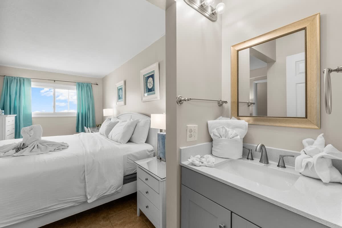 The Summit 1123 – Bedroom with queen bed, dresser, and bathroom vanity; window with blue sky view.
