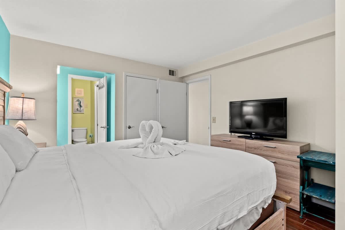 The Summit 731 – Bedroom with a large bed, TV, and colorful walls, leading to a bathroom door.