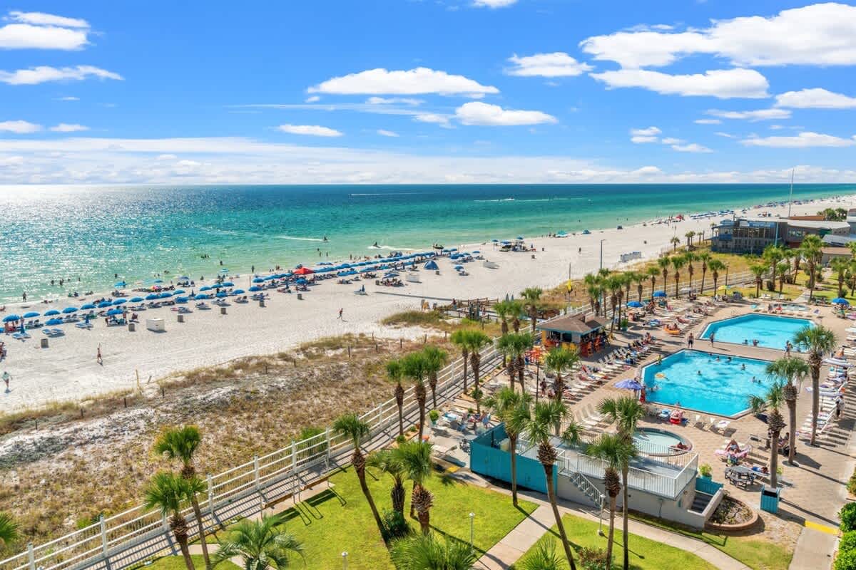 The Summit 731 – View of beach, pools, and palm trees under a blue sky with clouds.