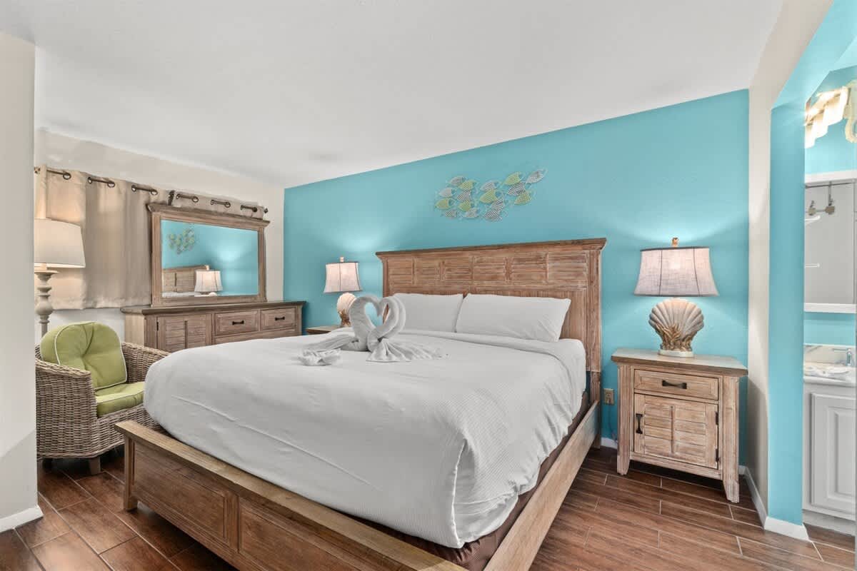The Summit 731 – Cozy bedroom with a wooden bed, blue accent wall, dresser, and a wicker chair.