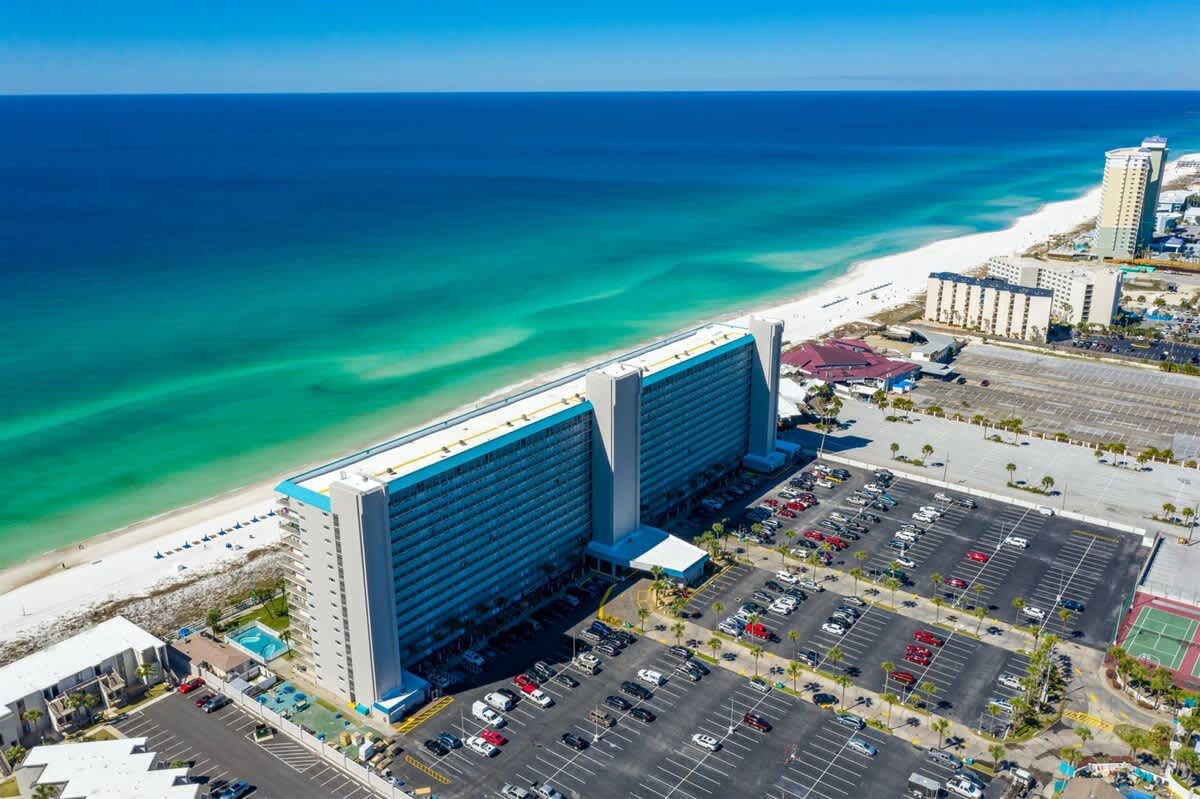 The Summit 731 – Aerial view of The Summit 731, beachfront location, parking lot, and surrounding buildings along a sandy beach.