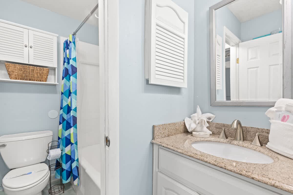 The Summit 712 – Bathroom with light blue walls, granite countertop, shower with colorful curtain, and white toilet.