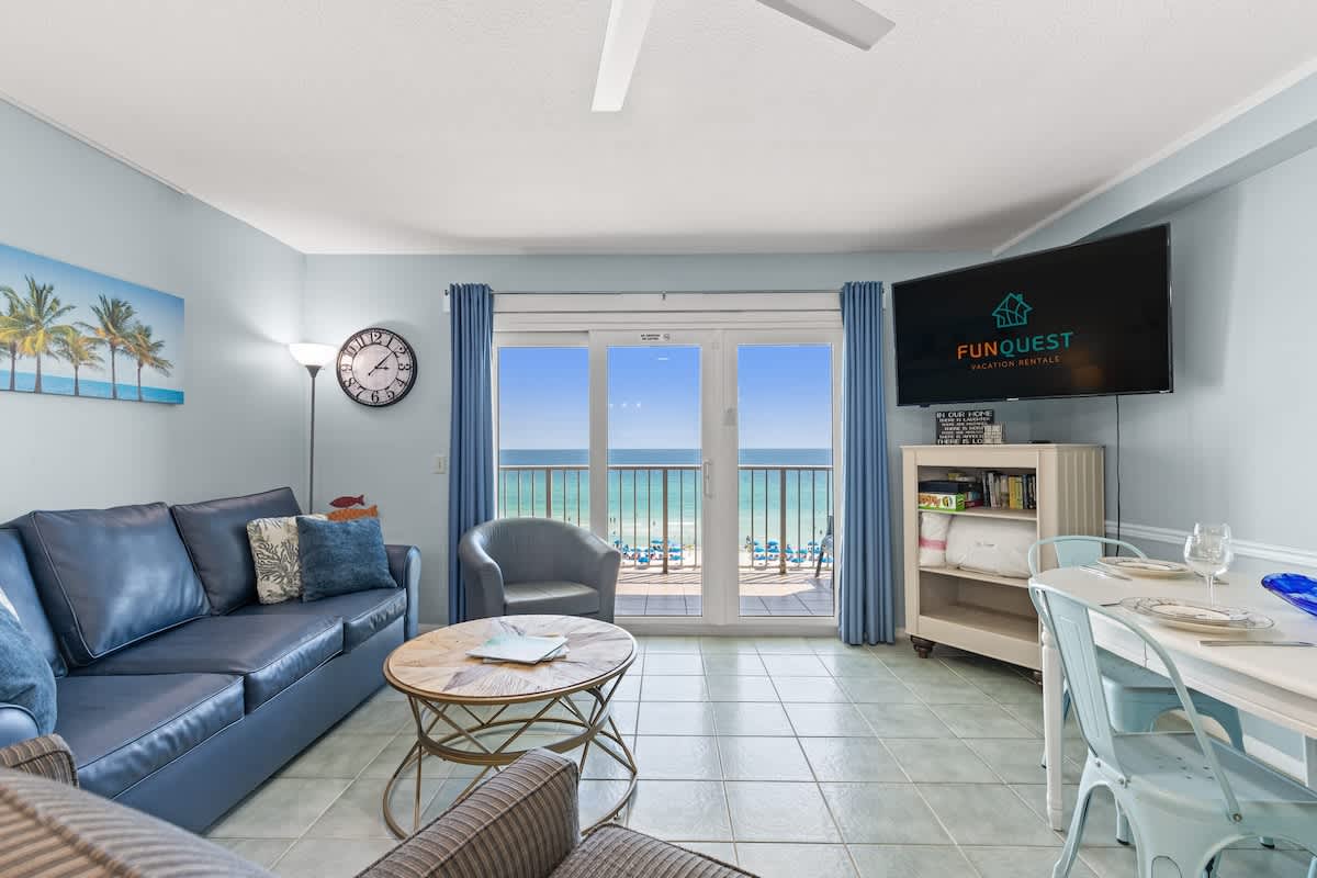 The Summit 712 – Living room with ocean view, sofa, chairs, and a dining table near large sliding glass doors.