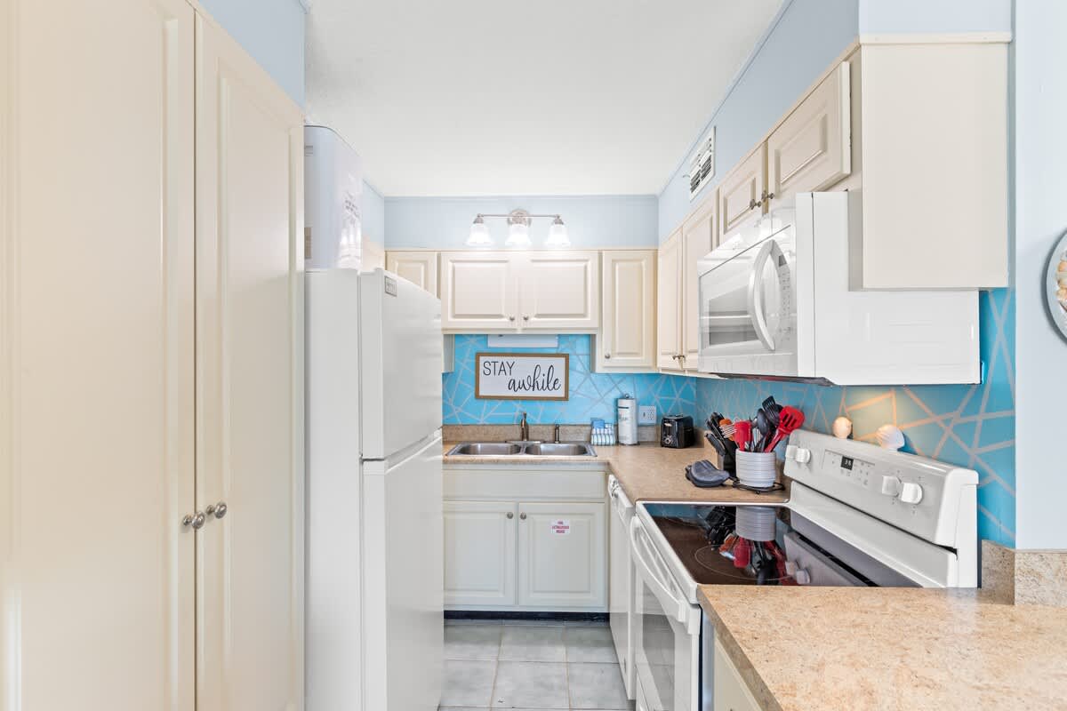 The Summit 712 – Kitchen with white appliances, light cabinets, blue backsplash, and countertop; small dining area visible.
