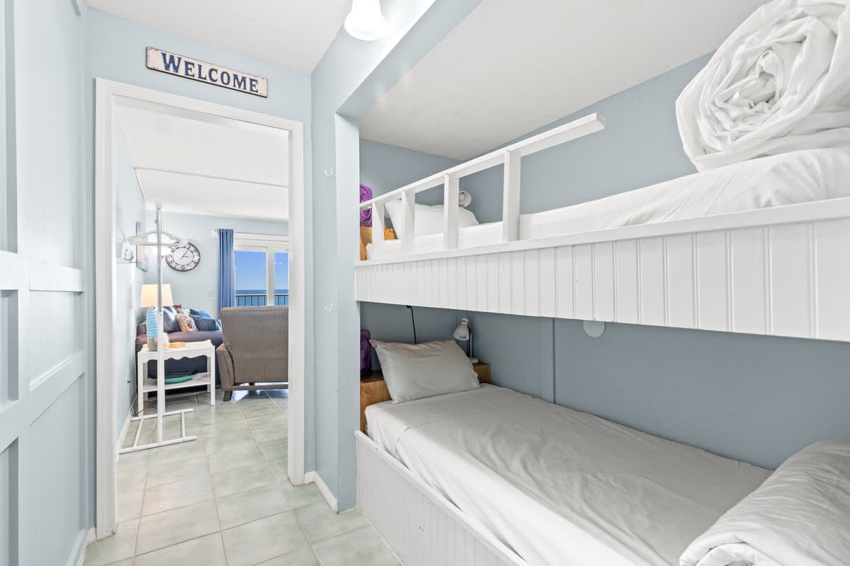 The Summit 712 – Bunk bed area with light blue walls, small lamp, and view of a living room and window.