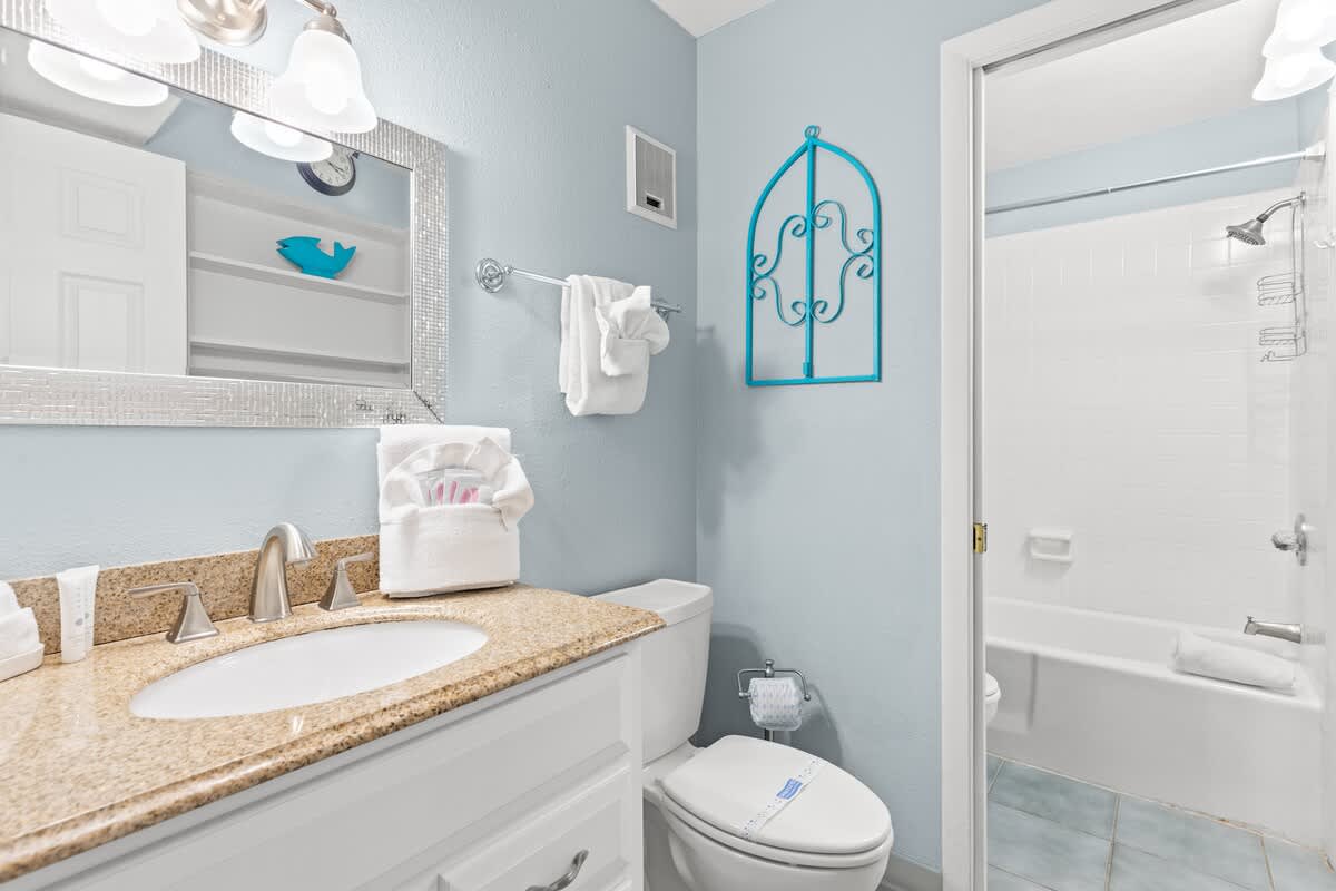The Summit 712 – Bathroom with granite countertop, white cabinetry, shower/tub combo, decorative blue accents, and plush towels.