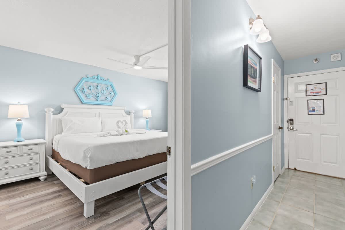The Summit 712 – Cozy bedroom with a king-size bed, blue accents, dresser, and entryway door.