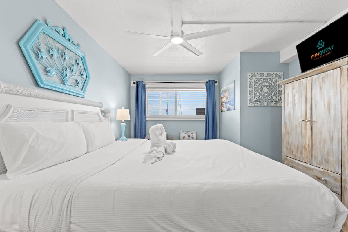 The Summit 712 – Cozy bedroom with a king bed, blue walls, decorative accents, and a window with blinds.