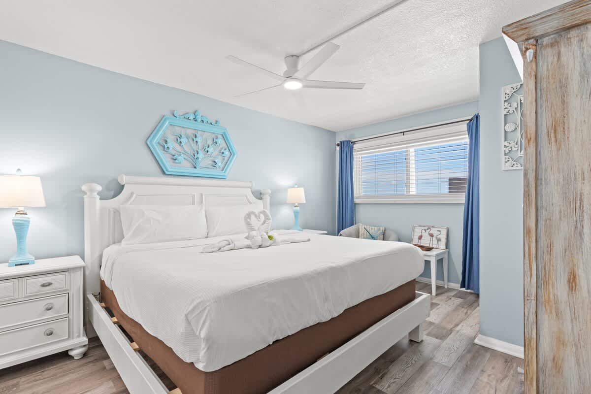 The Summit 712 – Bright bedroom featuring a king bed, nightstands, blue accents, and a window with blinds.