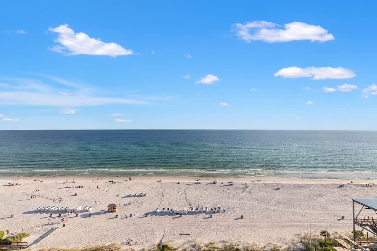 The Summit 1305 – Ocean view from balcony, sandy beach with sun loungers and people enjoying the water.