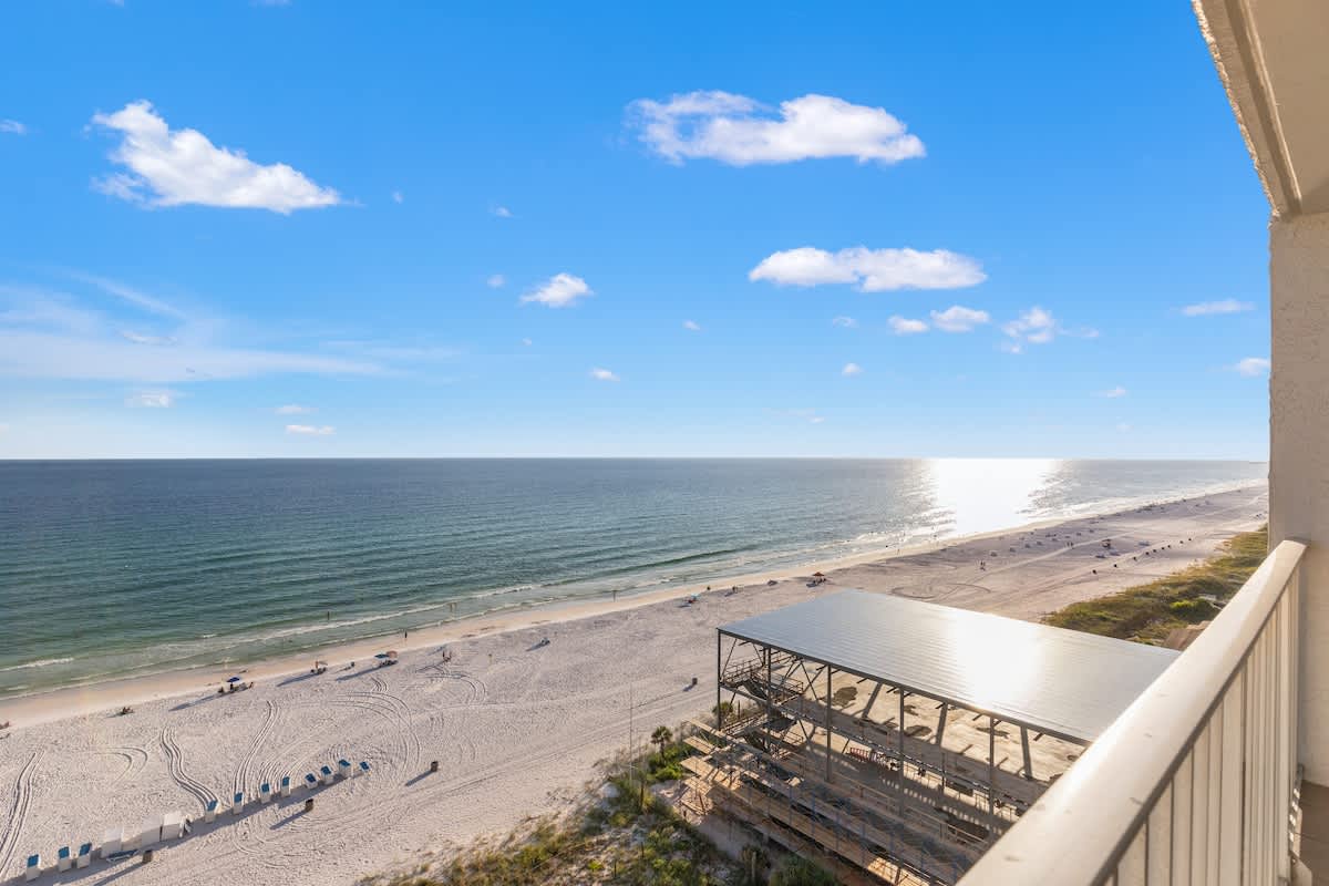 The Summit 1305 – Balcony view of a sandy beach and ocean under a blue sky with clouds.
