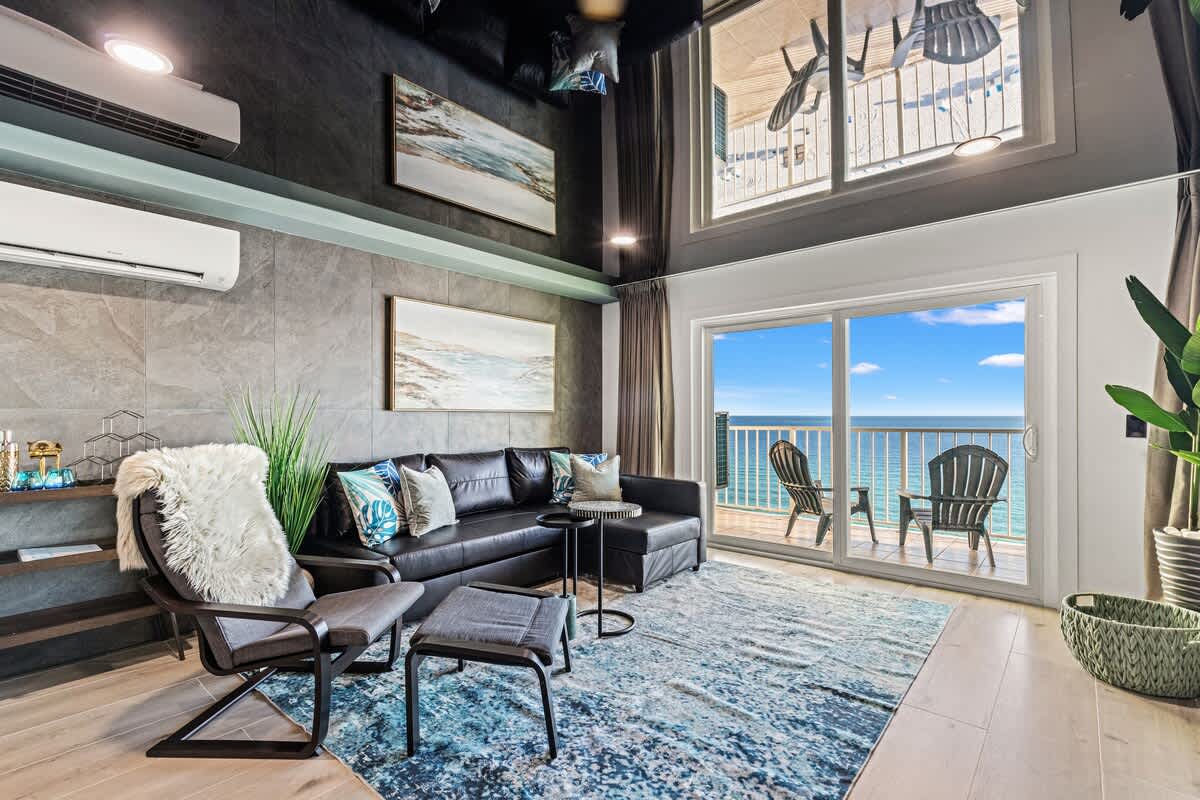 The Summit 1305 – Cozy living room with a balcony view of the ocean, featuring a black sofa and decorative art.