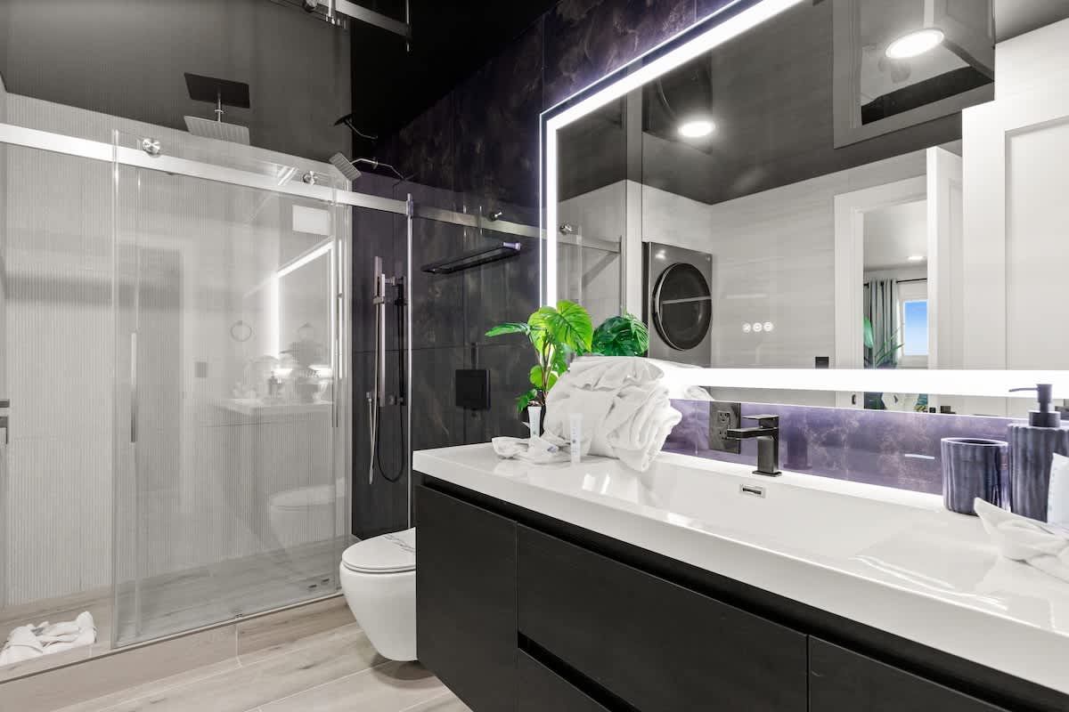 The Summit 1305 – Modern bathroom with a glass shower, vanity with mirror, and dark cabinetry.