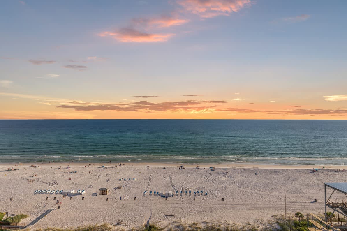 The Summit 1305 – Panoramic view of beach, ocean, and sunset with lounge chairs on white sand.