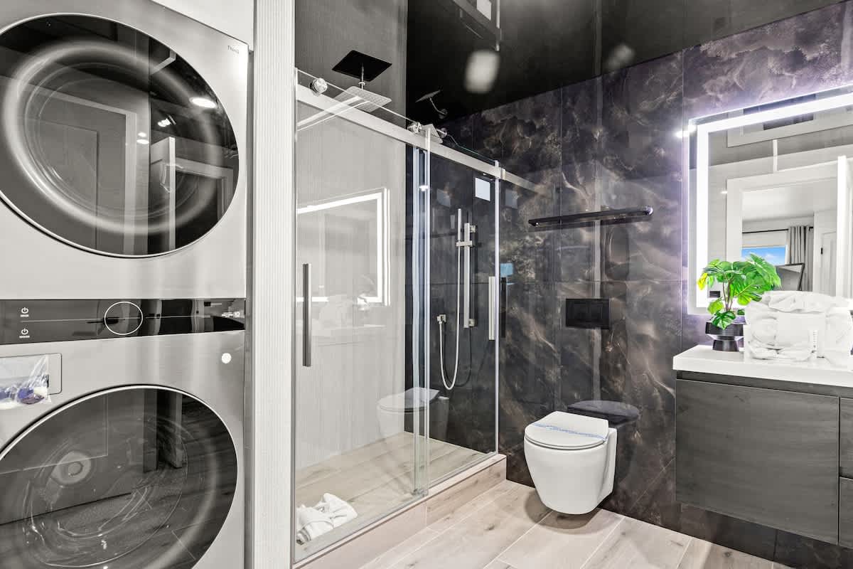 The Summit 1305 – Modern bathroom with a shower, washer and dryer, toilet, and a small plant on the countertop.