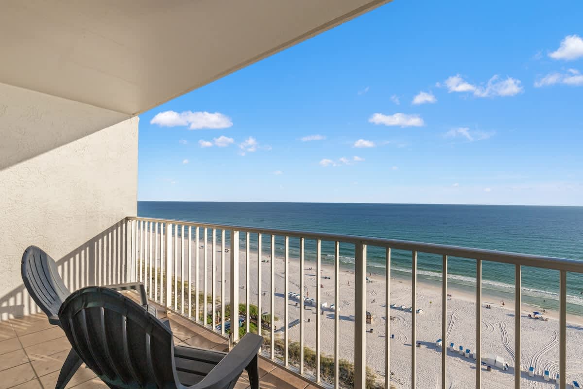 The Summit 1305 – Balcony view with two black chairs overlooking sandy beach and ocean under a clear blue sky.