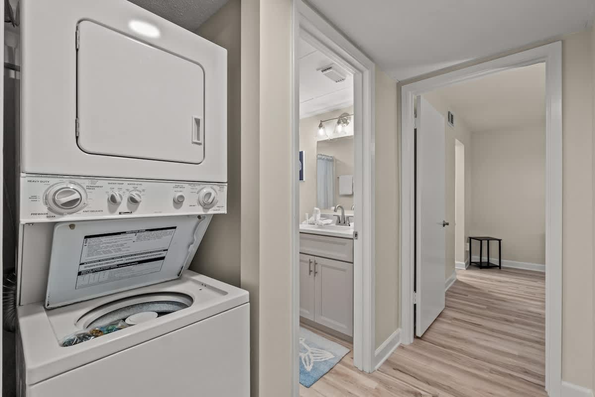 Aquavista 804E – Laundry area with stacked washer and dryer, doorways to bathroom and hallway, light wood flooring.