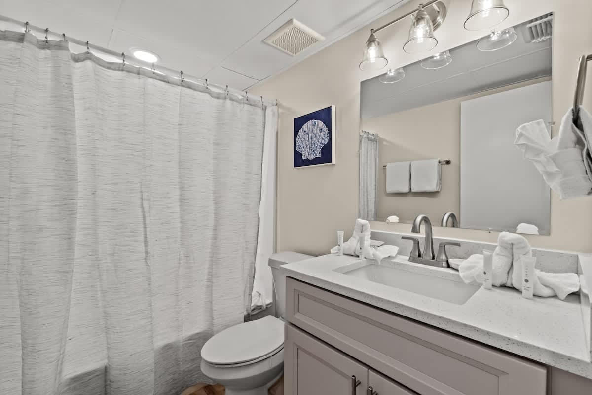 Aquavista 804E – Bathroom with a shower curtain, sink, mirror, toilet, and decorative shell artwork.