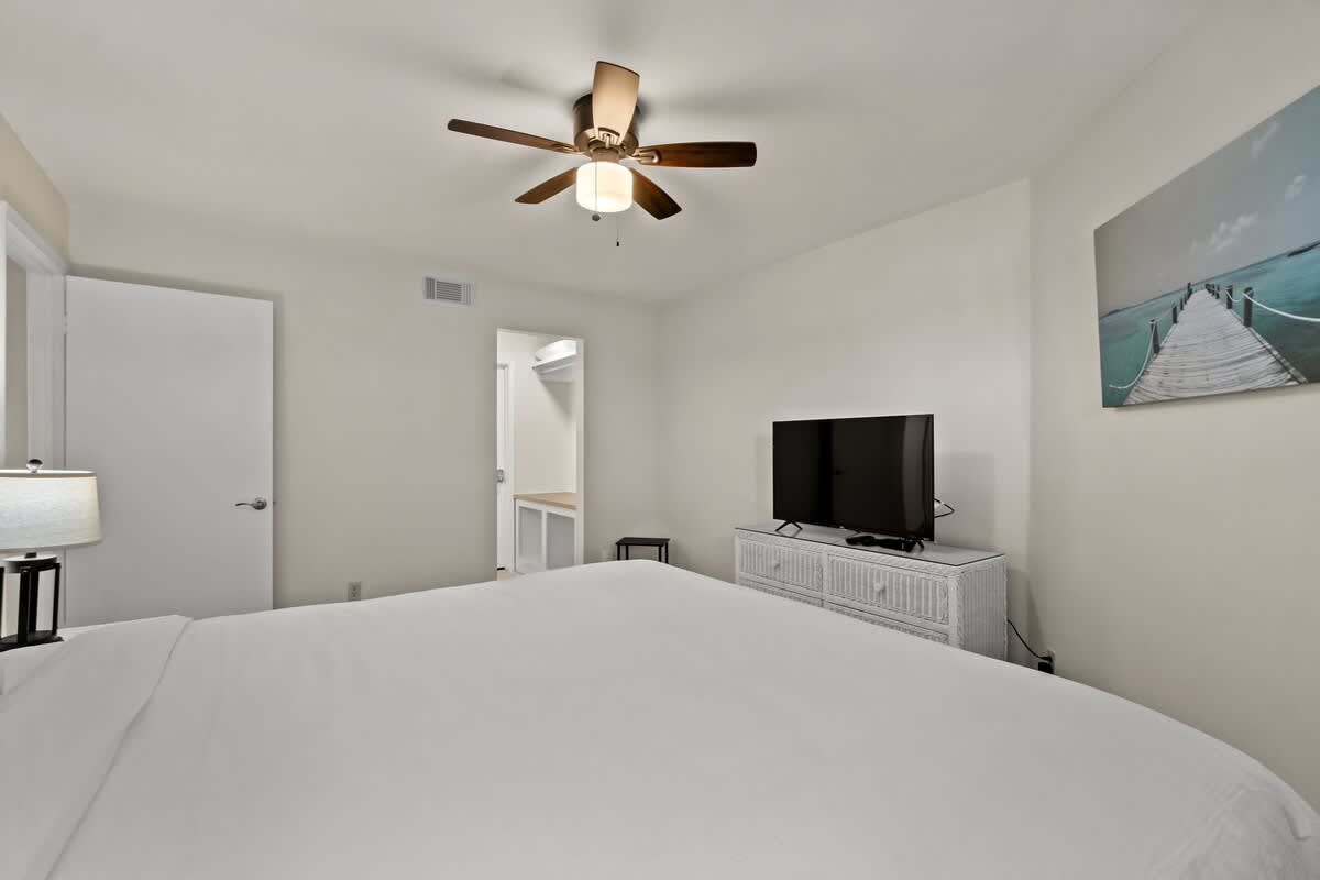 Aquavista 804E – Bedroom with queen bed, lighted ceiling fan, TV on a cabinet, and an adjoining closet area.